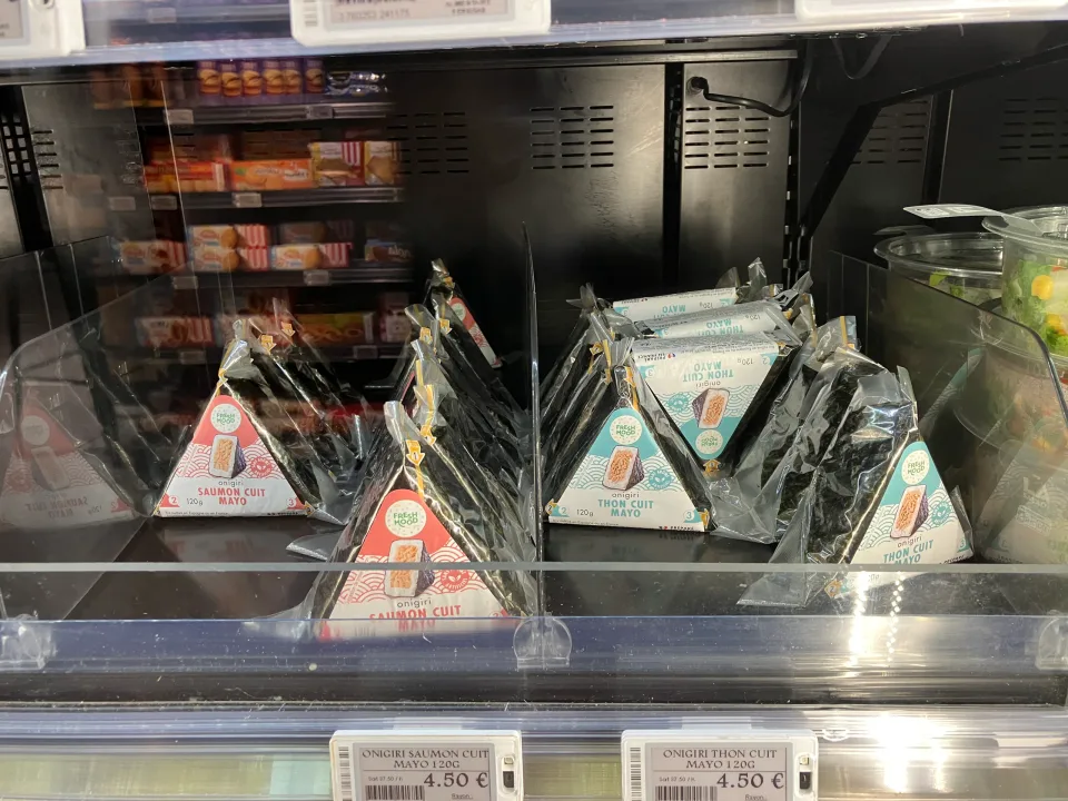 店の冷蔵棚に並ぶ三角形のパッケージに包まれたおにぎり