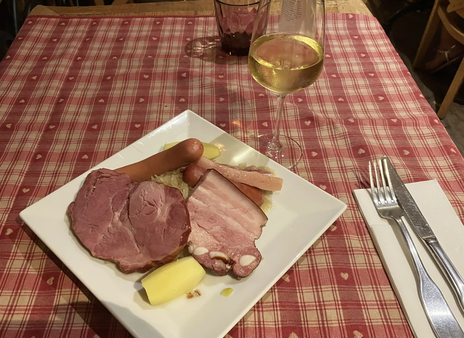 赤いチェック柄のテーブルで白ワインとともに供された肉とソーセージの料理